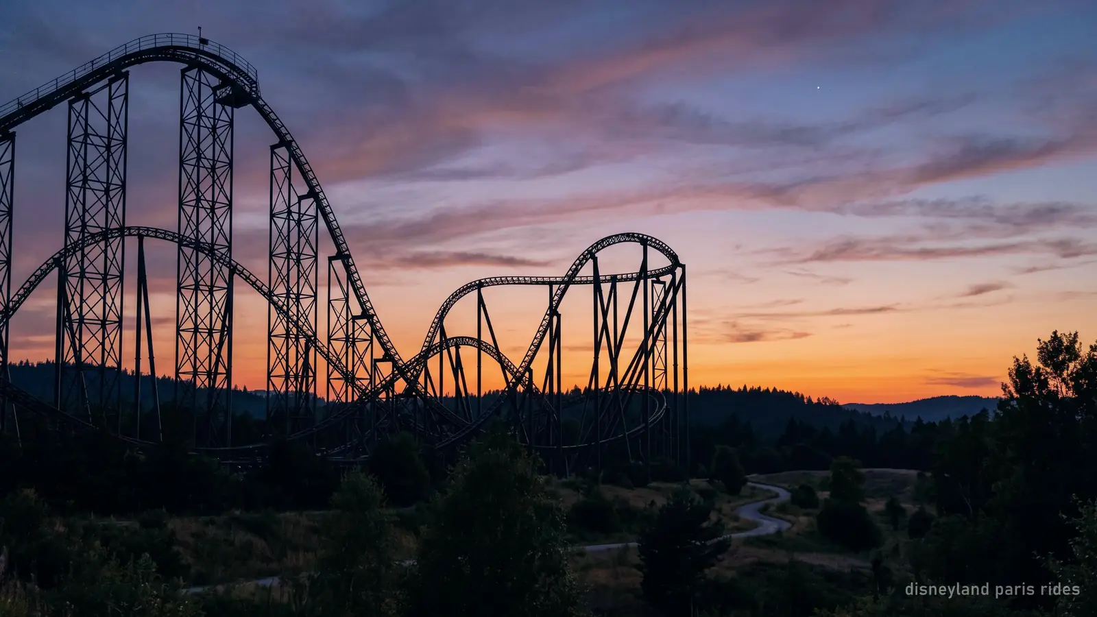 The silhouette of a steel roller coaster track against a dusk sky