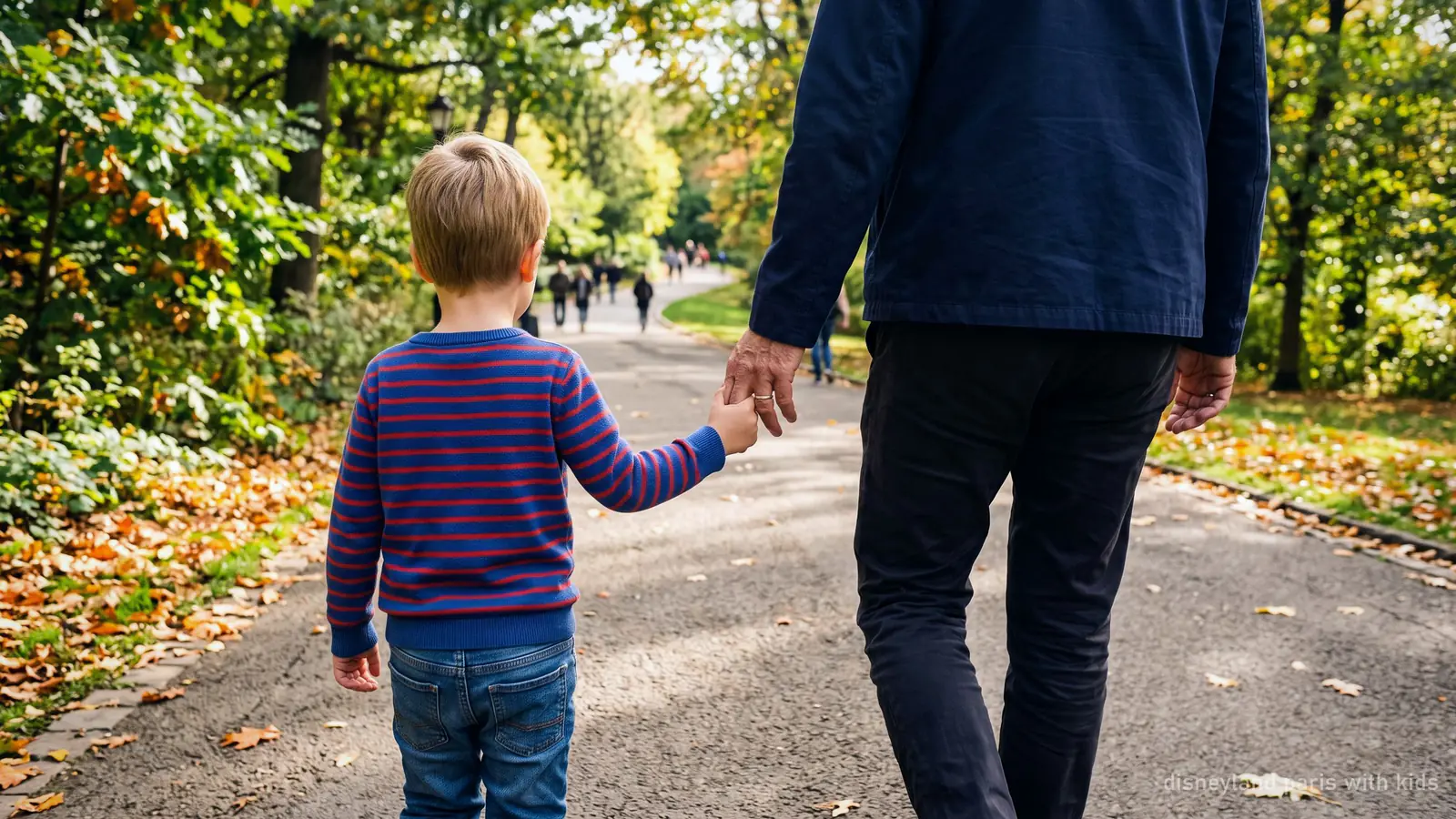 A child's hand held in an adult's hand on a paved park path, seen from behind