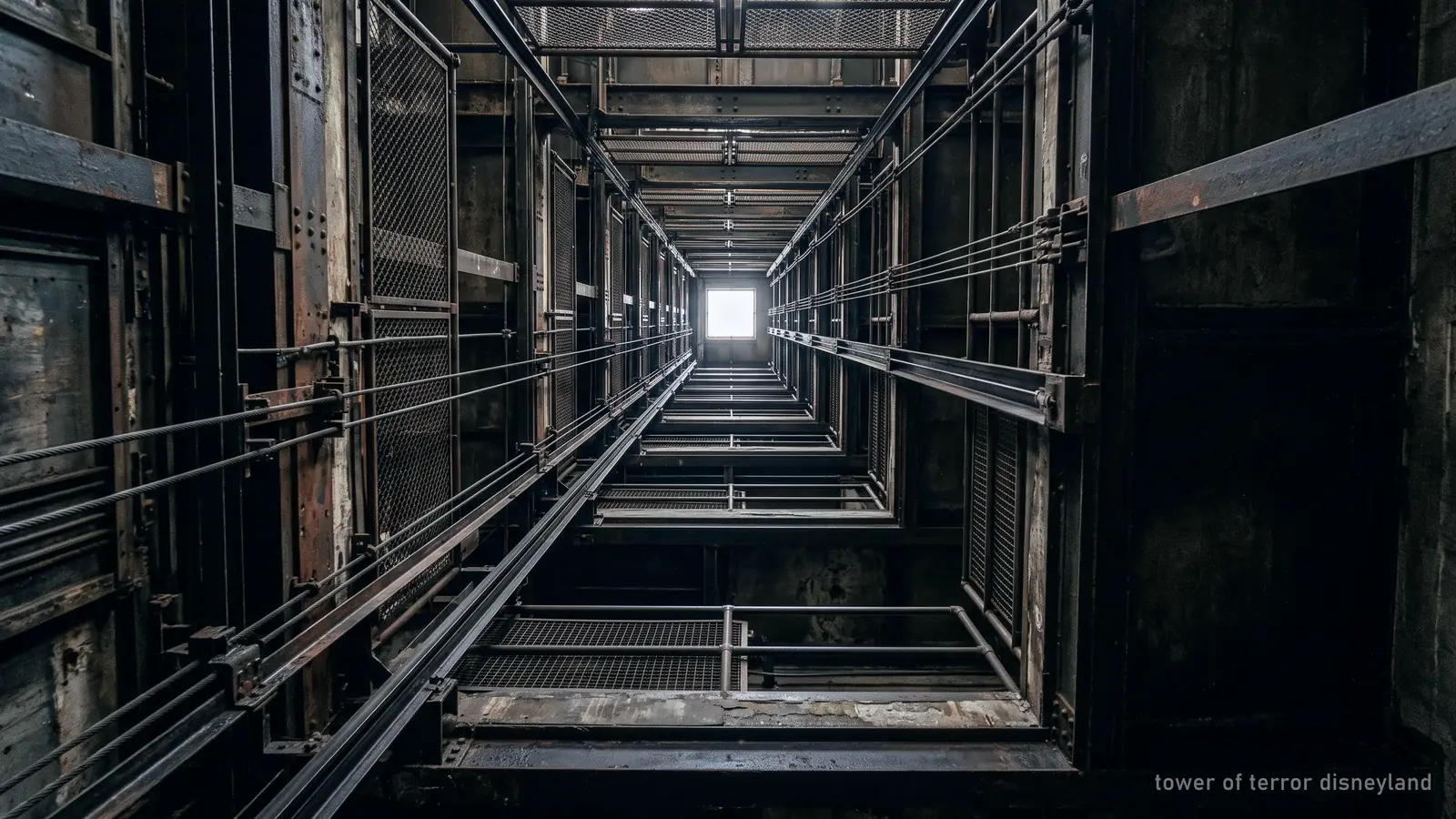 Looking straight up a tall lift shaft toward a small square of daylight far above